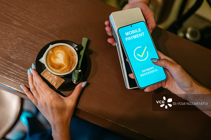 年轻女性在咖啡店通过移动银行应用进行非接触式支付图片素材