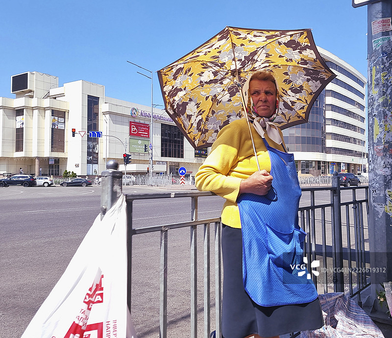 一位老年女性街头小贩撑着伞，保护自己免受阳光照射图片素材
