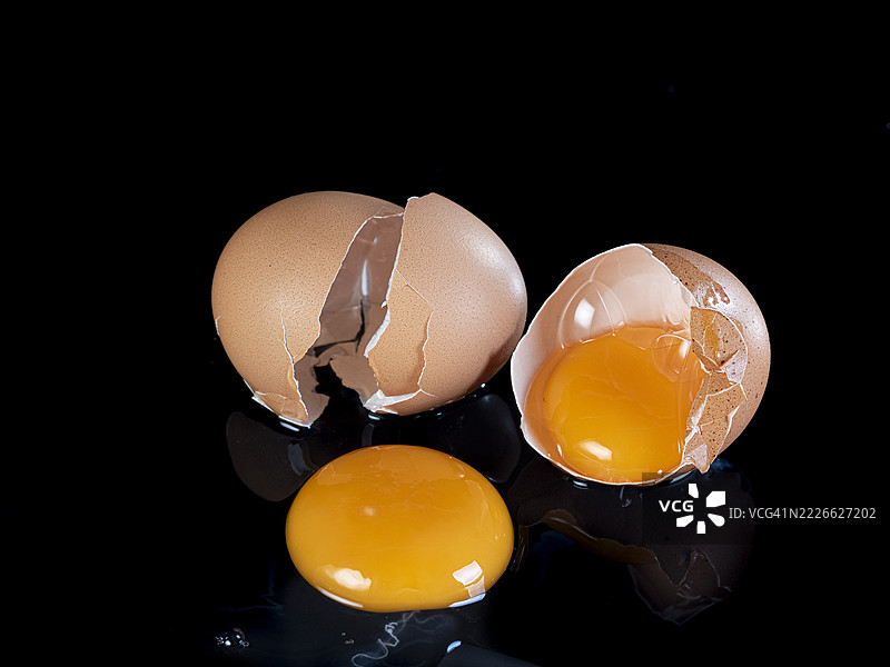 两个破碎的鸡蛋，蛋黄流出，背景为黑色。图片素材