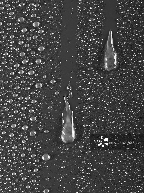 两滴水沿着湿润的灰色表面滑落。图片素材