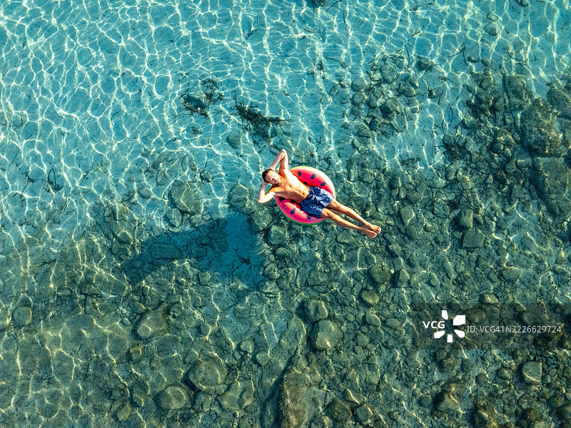 男子在清澈的水中放松，坐在充气圈上图片素材