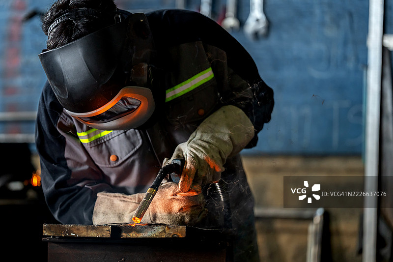 一位高技能的焊工在工厂中进行精确的金属焊接，焊接喷嘴飞溅出火花。该图像展示了先进的焊接技术、稳定的手部控制以及在工业工程和金属制造方面多年的实践经验。图片素材