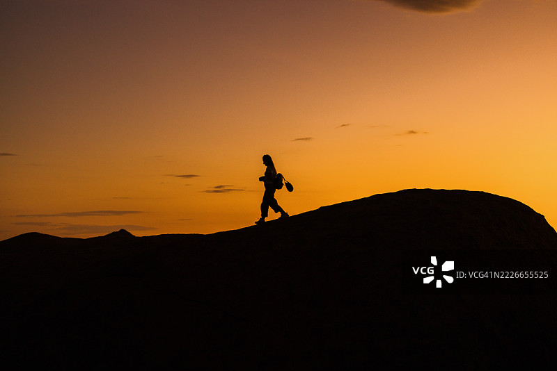 年轻女性在日落时分走在山丘上图片素材