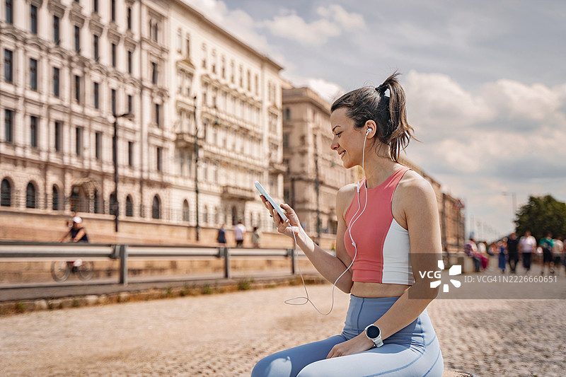 年轻的女运动员在训练后坐着使用手机图片素材