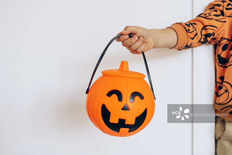 孩子的手握着万圣节南瓜糖果桶的特写，背景为白色。图片素材