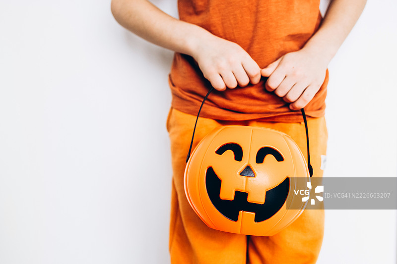 孩子的手握着万圣节南瓜糖果桶的特写，背景为白色。图片素材