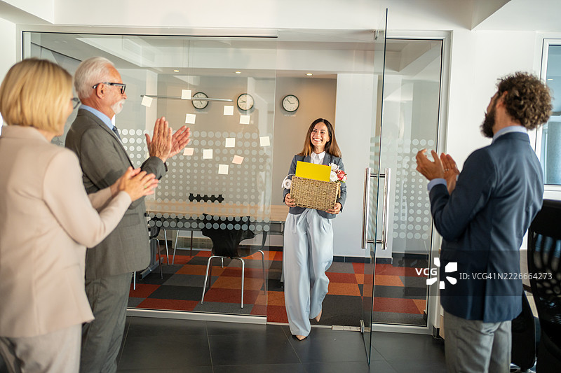 快乐的女商人辞职后离开办公室，同事们在鼓掌。图片素材