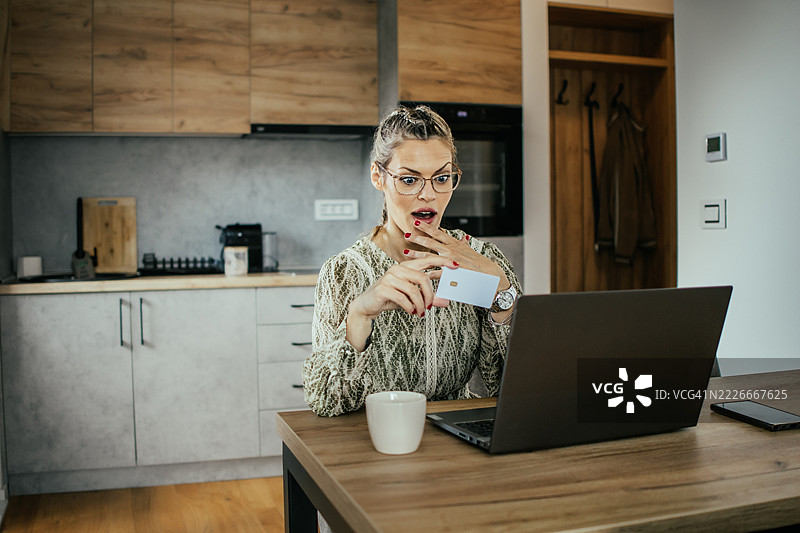 金发女子戴着眼镜，在现代公寓的笔记本电脑上使用银行信用卡进行在线购物，为家人购买礼物并支付账单。图片素材