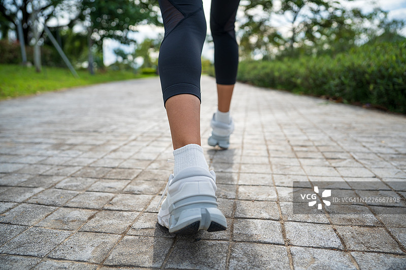 年轻女性跑者的脚在路上奔跑，鞋子特写。年轻女性的腿准备在路上跑步。女性在阳光明媚的日子里走在跑道上。女性在户外公园锻炼。户外健身。健康生活方式和身体活动的概念。图片素材