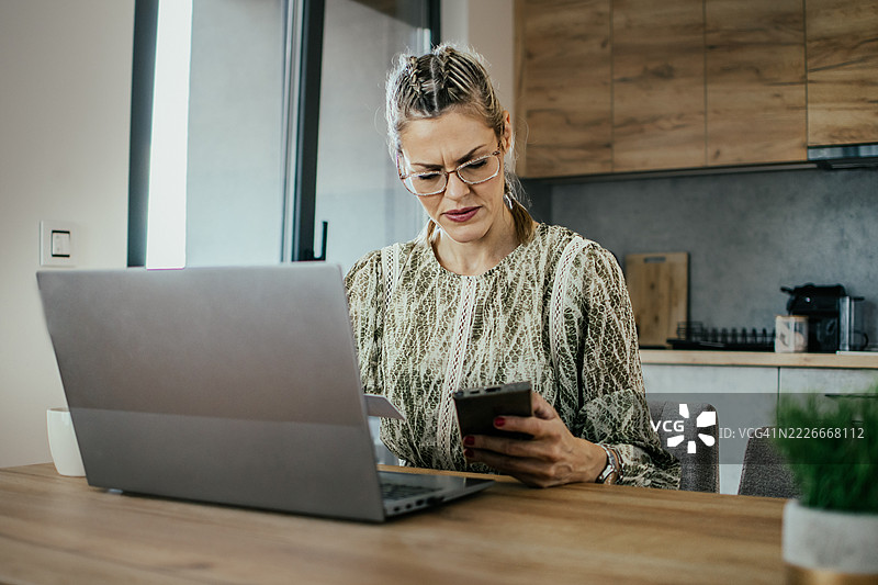 金发女子戴着眼镜，在现代公寓中使用笔记本电脑和银行信用卡进行在线购物，为家人购买礼物并支付账单。图片素材