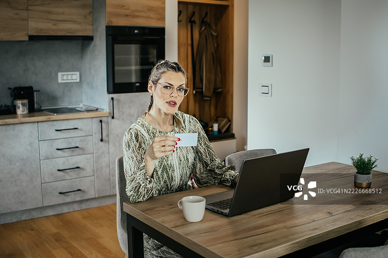 金发女子戴着眼镜，在现代公寓里用笔记本电脑使用银行信用卡进行在线购物，为家人购买礼物并支付账单。图片素材