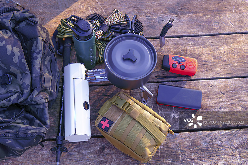 西班牙马拉加的隆达，基本露营装备包括背包、炊具、急救包和导航工具，整齐地摆放在一块风化的木质表面上。图片素材