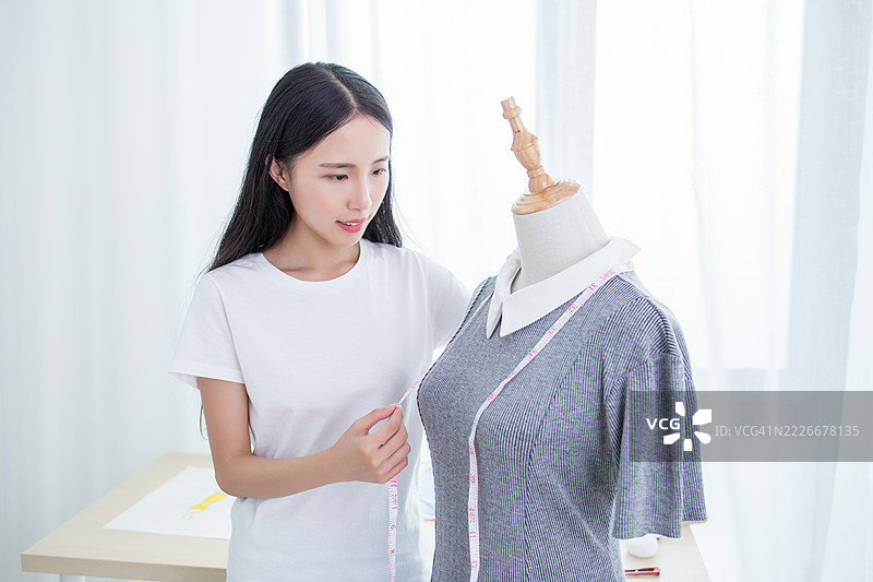 年轻女性在模特上测量裙子以进行时尚设计图片素材