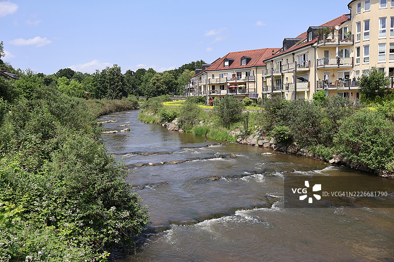 阳光明媚的乡村环境中，河边房屋旁的小溪流淌图片素材