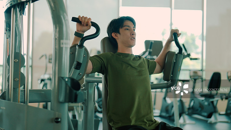 年轻的亚洲男子在健身房的器械上锻炼肩部肌肉。图片素材