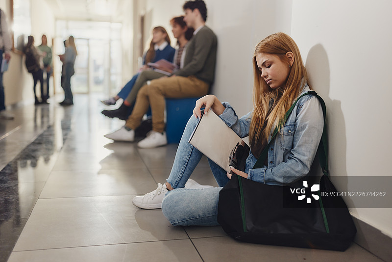 女学生在走廊的休息时间放松地躺在地板上。图片素材