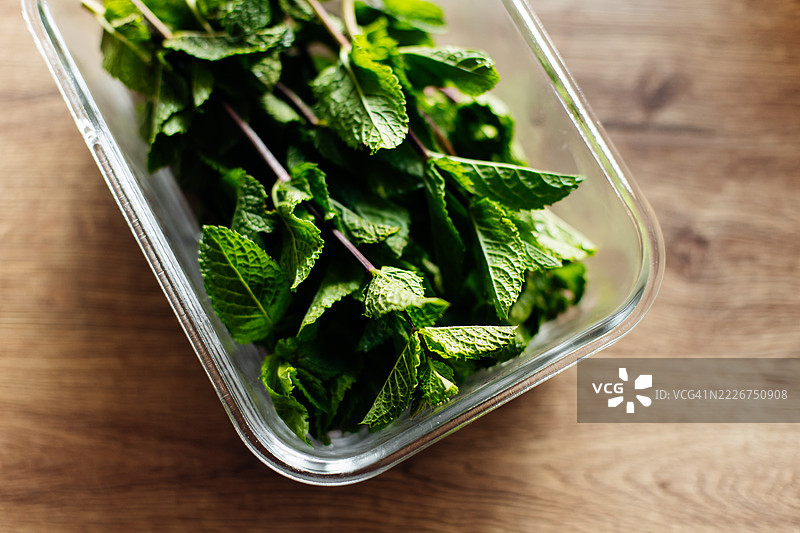 新鲜薄荷叶放在玻璃容器中，背景为木质纹理图片素材