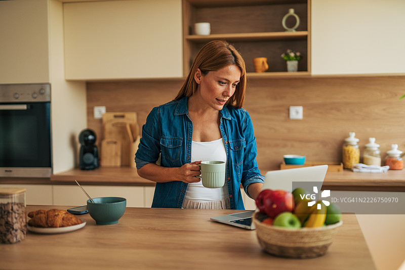 女人在厨房里一边吃早餐一边远程工作图片素材