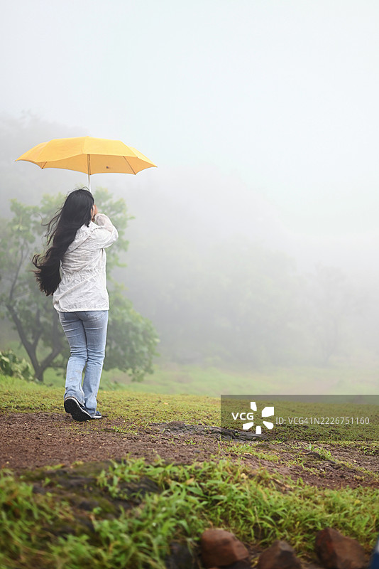 在自然中雾气弥漫的小径上，女人手持雨伞图片素材