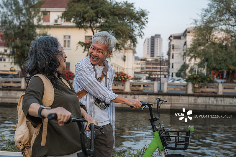 一对老年夫妇在城市中缓慢行走，推着他们的自行车，刚完成骑行。图片素材