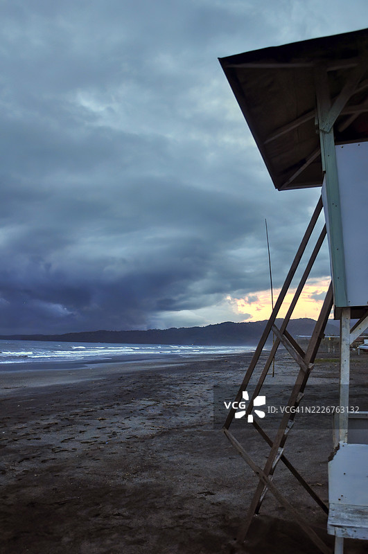 一座白色的救生员小屋，配有红色的救生圈和旗帜，矗立在黑暗的海滩上。图片素材