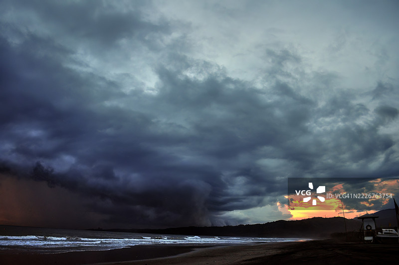 一幅戏剧性的海景，波涛汹涌，暴风云密布，地平线上散发着温暖的光辉。图片素材