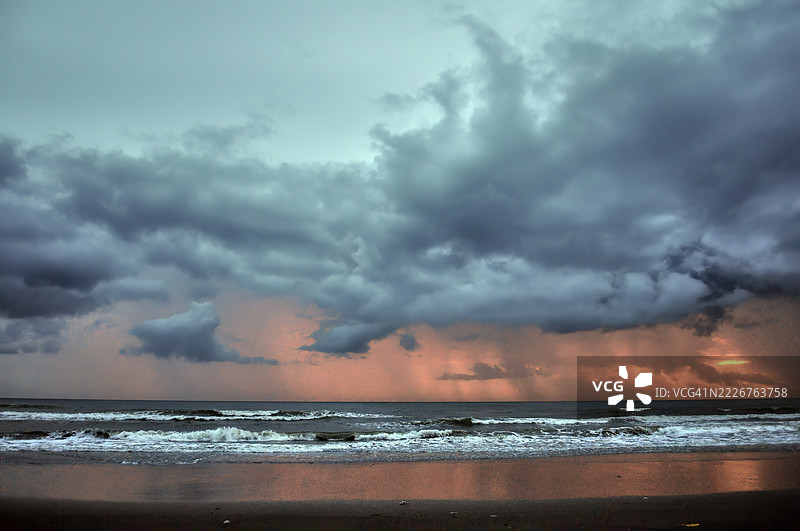 一幅戏剧性的海景，波涛汹涌，暴风云密布，地平线上散发着温暖的光辉。图片素材