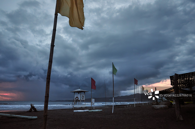 黎明或黄昏时分，阴暗暴风雨的海滩上，前景中有一根旗杆。图片素材