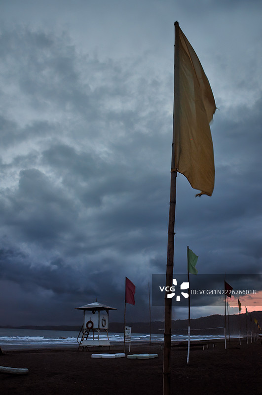 黎明或黄昏时分，阴暗暴风雨的海滩上，前景中有一根旗杆。图片素材