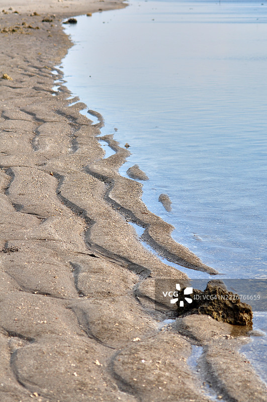 宁静的海岸线与平静的水面相接，边缘处泛起轻柔的涟漪。图片素材
