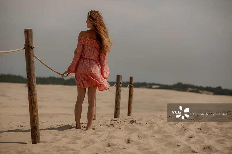 穿着飘逸红色连衣裙的女人在宁静的沙滩小径上漫步图片素材