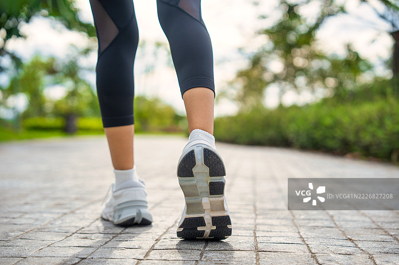 年轻女性跑者的脚在路上奔跑，鞋子特写。年轻女性的腿准备在路上跑步。女性在阳光明媚的日子里走在跑道上。女性在户外公园锻炼。户外健身。健康生活方式和身体活动的概念。图片素材