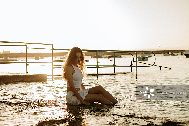 年轻女性在日落时分海边放松，享受宁静的风景图片素材