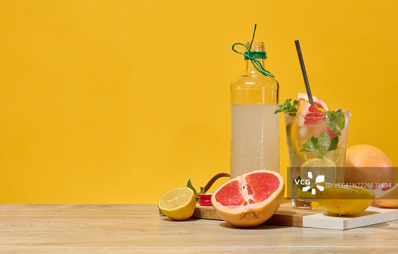 新鲜的柑橘饮料，含有柠檬、葡萄柚和薄荷，装在冰块和吸管的玻璃杯中，周围是新鲜的柑橘水果和一瓶自制柠檬水，乌克兰图片素材