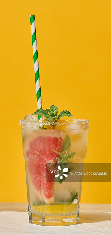 一杯清澈的玻璃杯，装有冷饮，配有葡萄柚片、冰块、薄荷和柠檬，带有绿色条纹的吸管，乌克兰图片素材