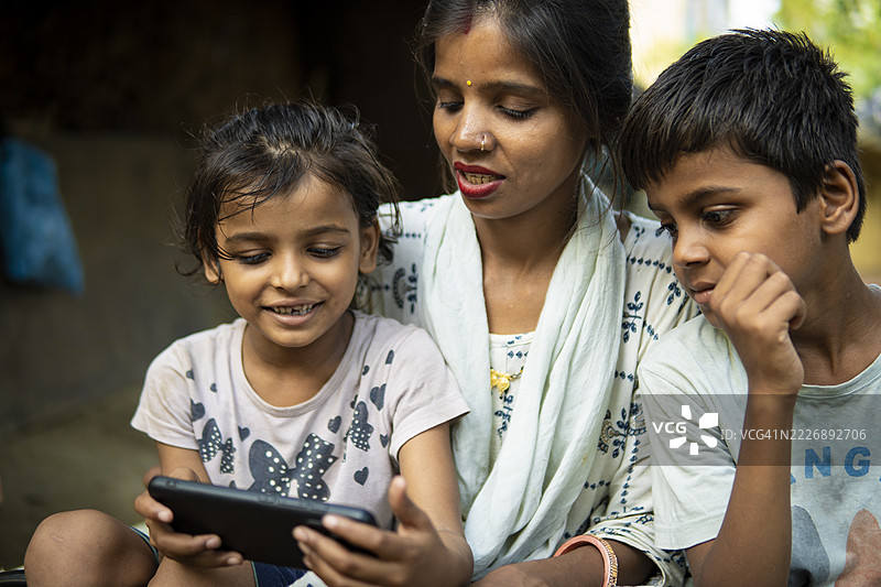 快乐的印度乡村母亲和她的儿女坐在一起使用智能手机。图片素材