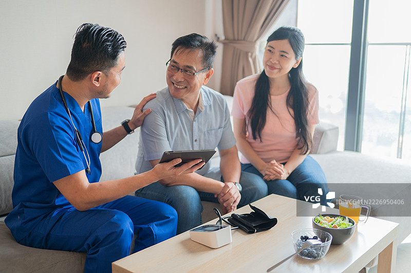关心的男性护士使用平板电脑向在家中的老年男性及其女儿解释健康状况的照片图片素材