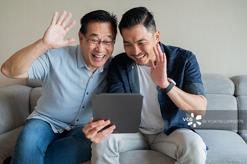 亚洲父亲与儿子使用数字平板进行海外父母视频通话的照片图片素材