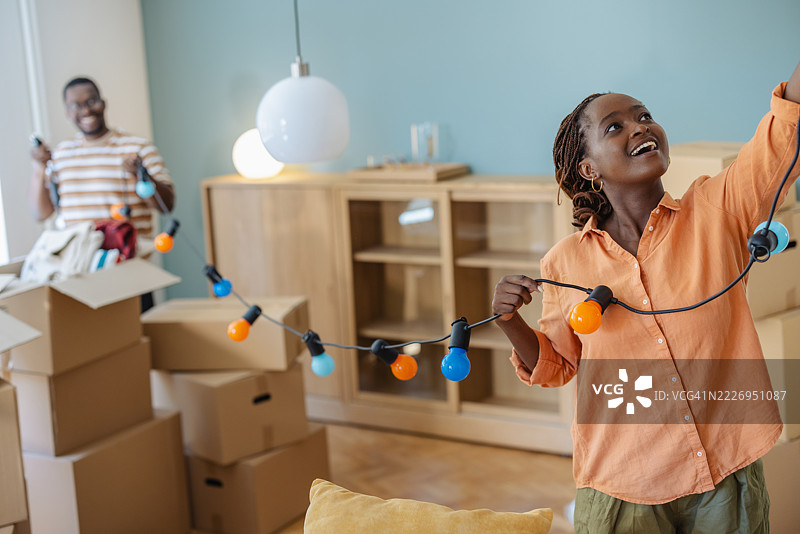快乐的情侣在新家里用串灯装饰并拆箱子图片素材