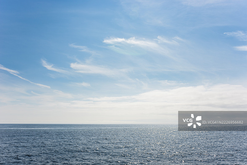 在晴朗的蓝天下,黑暗的海洋与明亮的白色羽毛状云朵相映成趣,云层、地平线、水面上的光线反射,深蓝色、光线、反射、阳光、海面、夏季、晴朗的天气、平静的海洋、广阔的地平线、风景、海洋、自然。图片素材