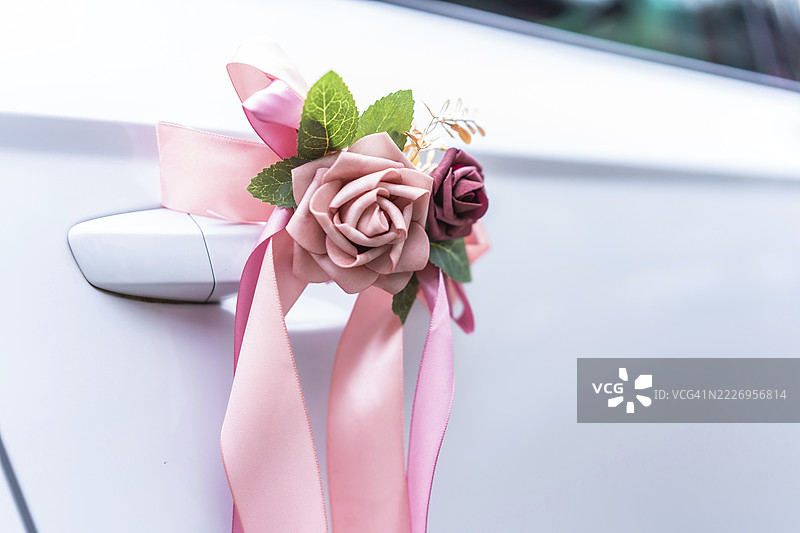 优雅的粉色丝带和人造花装饰着白色汽车的把手，象征着婚礼庆典。图片素材