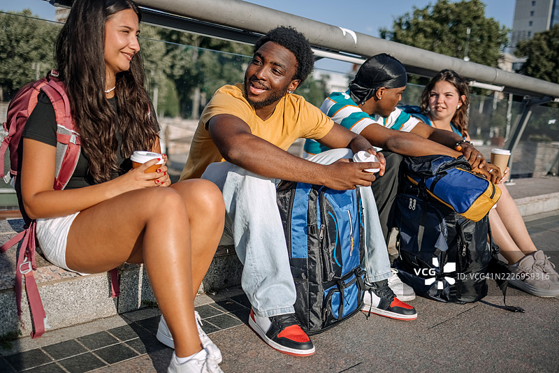 一群背包客在城市的桥上坐着休息，喝着咖啡。图片素材