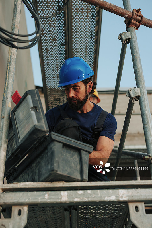 建筑工人在脚手架上寻找工具箱中的工具图片素材