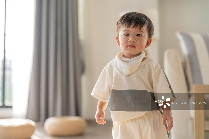 亚洲小男孩穿着休闲服装，微笑着享受美好的一天，在客厅的木地板上快乐地玩耍，尽情走动，洋溢着幸福的婴儿时刻。图片素材