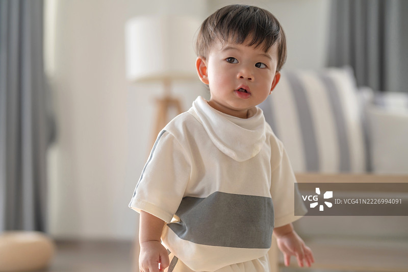 亚洲小男孩穿着休闲服装，微笑着享受美好的一天，在客厅的木地板上快乐地玩耍，尽情走动，洋溢着幸福的婴儿时刻。图片素材