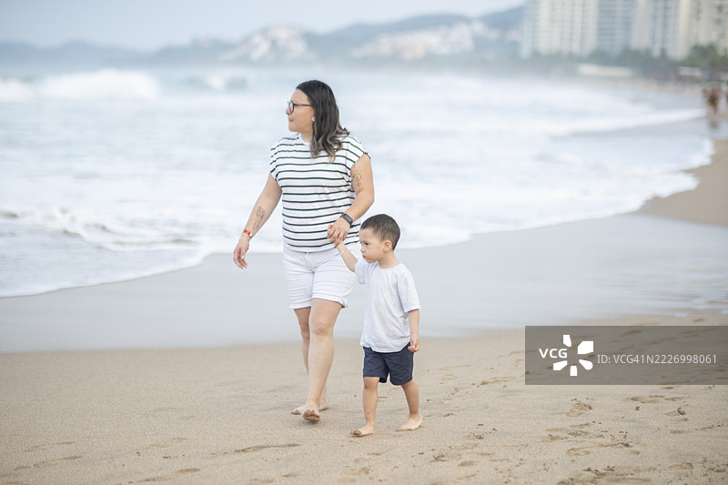 母亲和儿子在美丽的墨西哥海滩度假，沿着海边的沙滩散步。图片素材