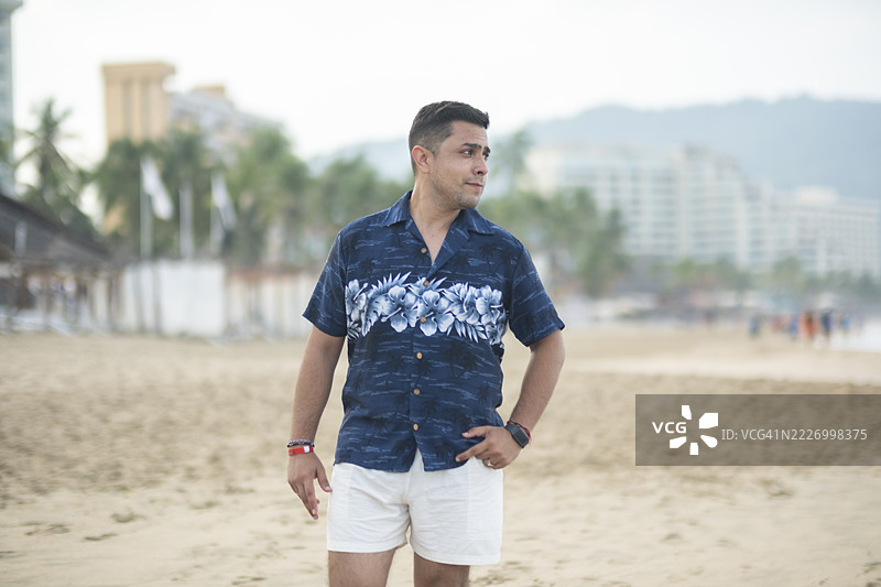 年轻男子在美丽的墨西哥海滩度假，边走边摆姿势拍照。图片素材