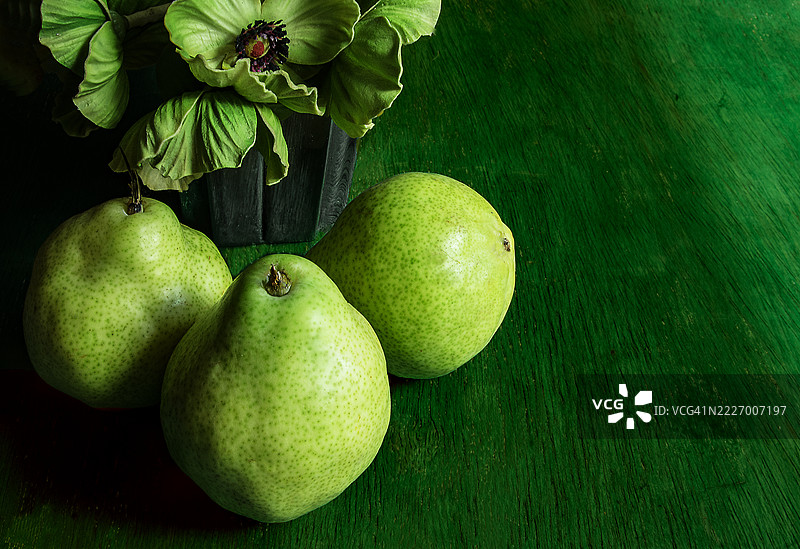 三个非常绿色的梨子旁边放着一个装有绿色牡丹的花瓶。绿色背景。图片素材