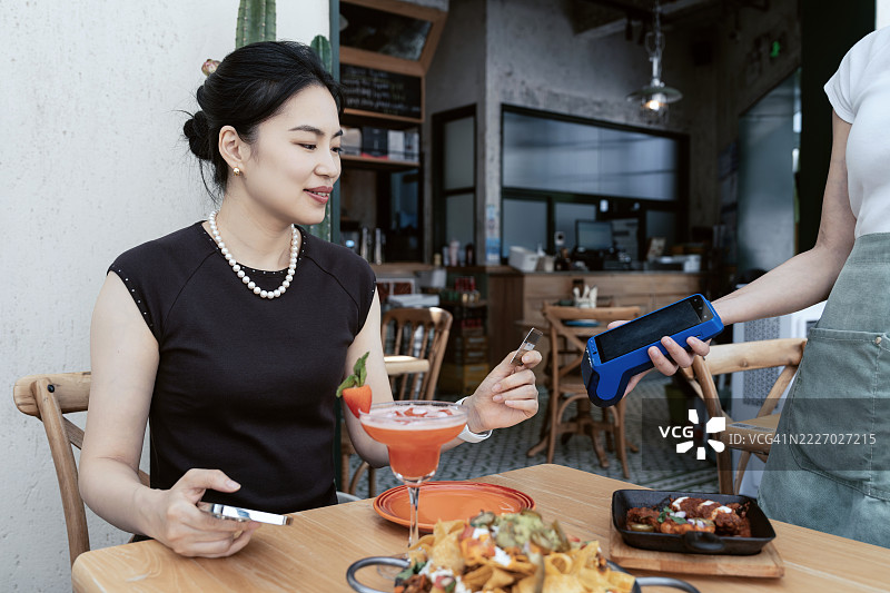 美丽的年轻亚洲女性在餐厅用智能手机进行移动支付。图片素材
