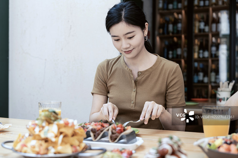 年轻的亚洲女性在餐桌上享用一块多汁的烤牛排，旁边还有各种菜肴。图片素材